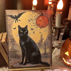 May include: A black cat sits on a wooden platform in front of a vintage Halloween-themed illustration. The illustration features a full moon, a bat, a pumpkin, and a cityscape. The cat is looking directly at the viewer.