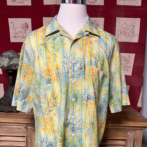 May include: A yellow and blue striped short-sleeved shirt with a floral print. The shirt has a button-up collar and a pocket on the left side.