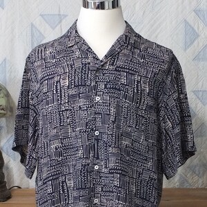May include: A navy blue short-sleeved button-up shirt with a white geometric pattern.