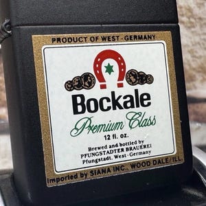 May include: Black lighter with a label featuring the text "Bockale Premium Class" and a horseshoe design. The label also includes the text "Product of West-Germany" and "12 fl. oz."