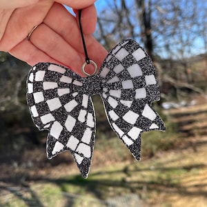 May include: A black and white checkered bow ornament with glitter. The bow is attached to a black string with a silver ring.