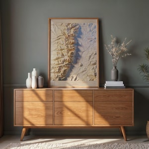 May include: A mid-century modern wooden sideboard with six drawers and tapered legs. A framed topographical map hangs above the sideboard. Decorative vases, books, and a potted plant complete the room's decor.