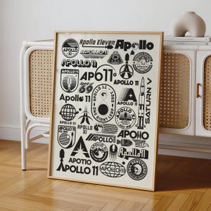 May include: A framed poster featuring a collection of black graphic designs, logos, and typography related to the Apollo 11 mission. The artwork includes various illustrations of rockets, lunar modules, globes, and text such as Apollo 11 and Saturn V.