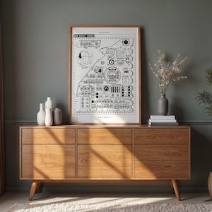 May include: A framed black and white blueprint-style print titled "NEW DISPLAY CONSOLE" sits atop a light brown wooden dresser. The dresser has six drawers and is flanked by decorative vases, books, and a potted plant. The room has a neutral color palette.