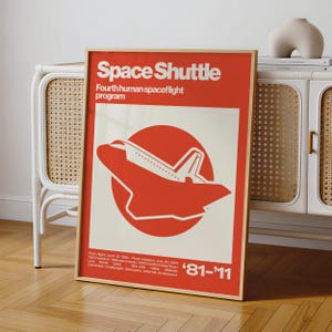 May include: A rectangular poster in a light wood frame featuring a red background with white text reading Space Shuttle Fourth human spaceflight program. A white silhouette of a space shuttle is centered over a red circle with '81-'11 at the bottom.