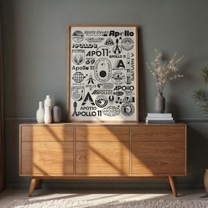 May include: A framed poster featuring various Apollo mission logos and text, displayed above a wooden cabinet. The cabinet has six drawers and is made of light-colored wood. Decorative vases and a plant are also visible.