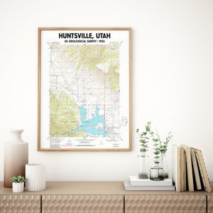 May include: A framed map of Huntsville, Utah, from the US Geological Survey in 1955. The map features topographical details in shades of green, brown, and blue, with the text "Huntsville, Utah" at the top. The frame is a light brown color.
