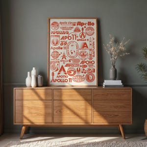 May include: A framed print featuring various red Apollo 11-themed stamps and logos. The print is displayed on a wooden mid-century modern style dresser. Decorative vases and a plant in a woven basket complete the room's decor.