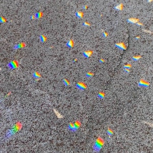 May include: A close-up of a gray, textured surface with many small, colorful rainbow-like reflections scattered across it.