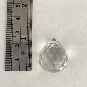 May include: A clear glass crystal prism pendant, approximately 1 inch in diameter, with a faceted design. The pendant is shown next to a ruler for size reference.