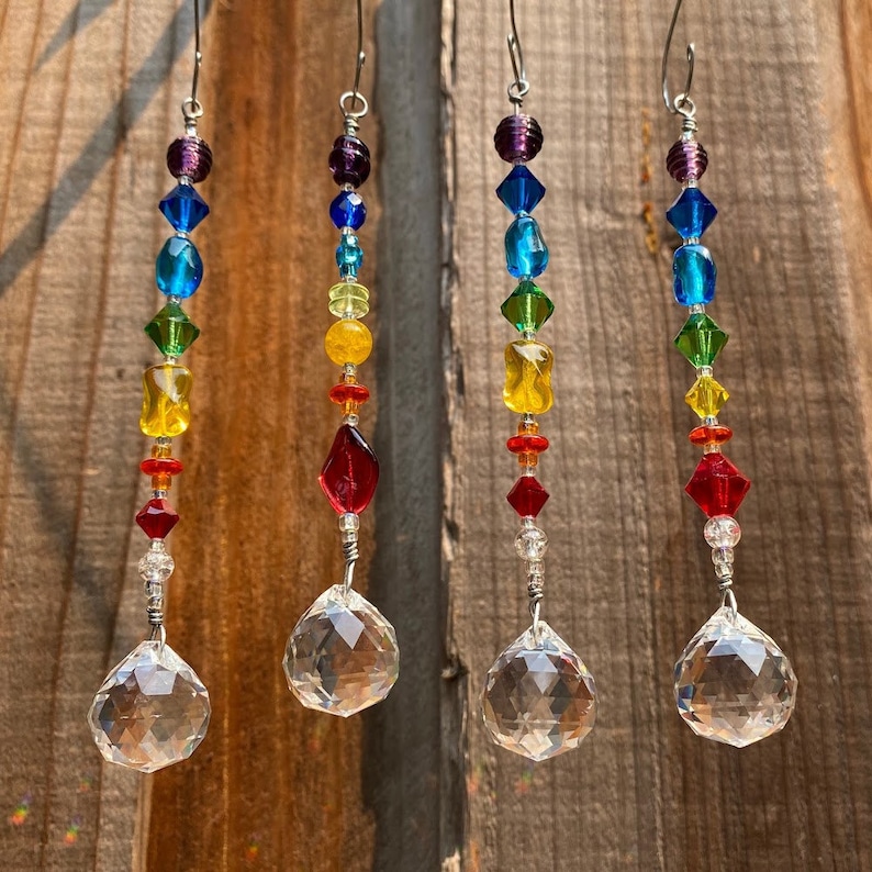 May include: Four rainbow crystal suncatchers with clear crystal prisms hanging from silver wire. Each suncatcher features a beaded strand of purple, blue, green, yellow, orange, and red beads.