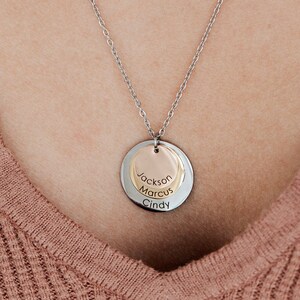 May include: A silver chain necklace with a round pendant featuring three names: Jackson, Marcus, and Cindy. The pendant is made of two overlapping circles, one silver and one gold.