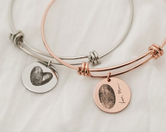 Puede incluir: Dos pulseras de brazalete ajustables. Una es plateada, la otra es de oro rosa. Cada pulsera tiene un dije redondo. Un dije tiene una huella en forma de corazón, el otro tiene una huella dactilar y la frase "Love, Mom".