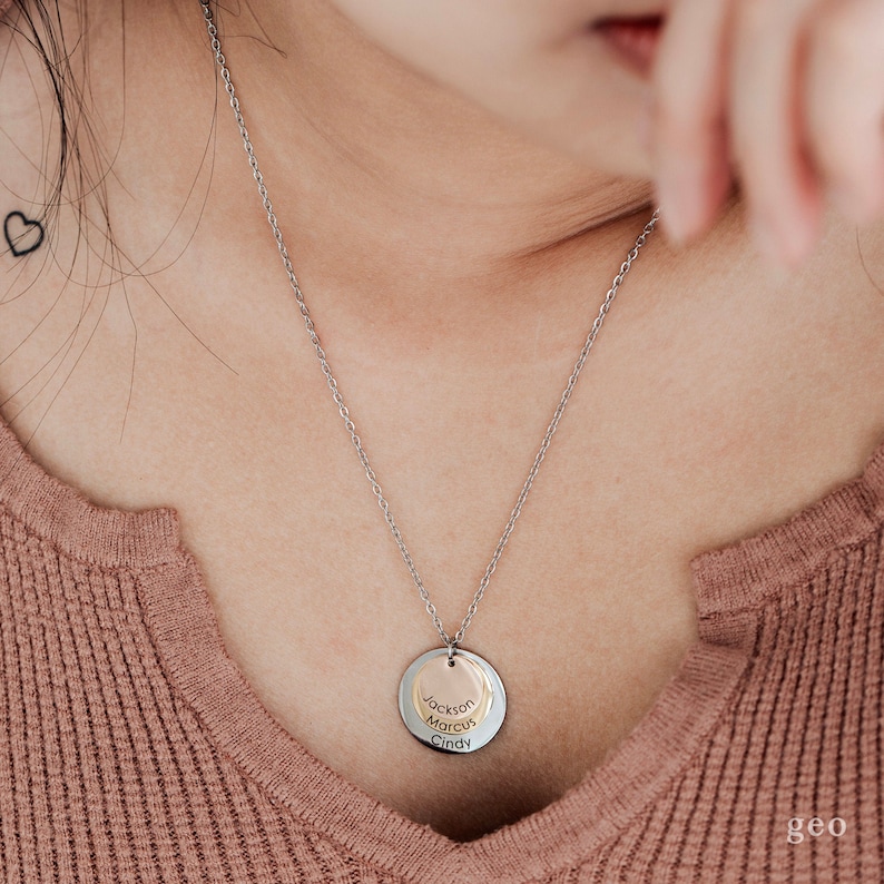 May include: A silver chain necklace with a round pendant featuring three names: Jackson, Marcus, and Cindy. The pendant is made of two overlapping circles, one silver and one gold.