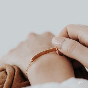 May include: A gold-toned bracelet with a thin, flat bar engraved with the Roman numerals "XIV" and "MMXIX".