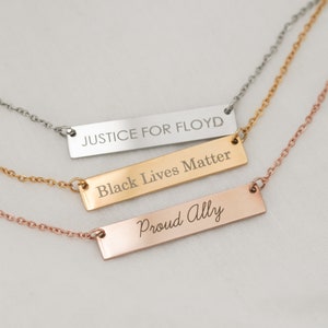 May include: Three silver, gold, and rose gold necklaces with bar pendants. The pendants are engraved with the phrases "Justice for Floyd", "Black Lives Matter", and "Proud Ally".