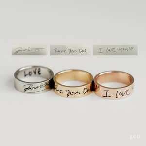 May include: Three rings in silver, gold, and rose gold. Each ring has a handwritten inscription. The silver ring says "LOVE" and has a signature. The gold ring says "Love you Dad". The rose gold ring says "I love".