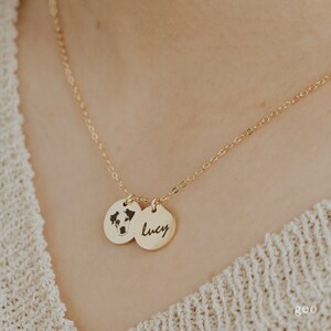 Op de afbeelding: Gouden ketting met twee ronde hangers. Een hanger heeft een zwart-wit foto van een hond, de andere hanger heeft de naam "Lucy" gegraveerd.