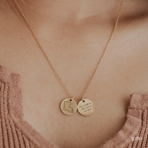 May include: Gold necklace with two round pendants. One pendant features the outline of the state of Louisiana. The other pendant has the text "Met in California, Fell in love in New York".