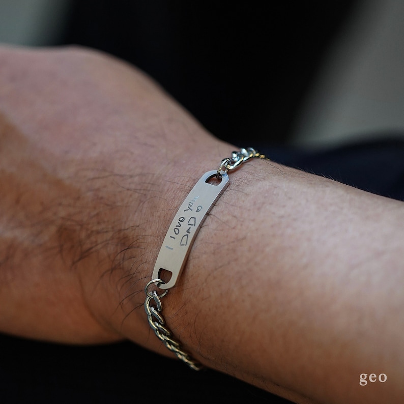 Puede incluir: Un brazalete de cadena de plata con una etiqueta rectangular que dice "Te amo pap&aacute;" en escritura manuscrita.