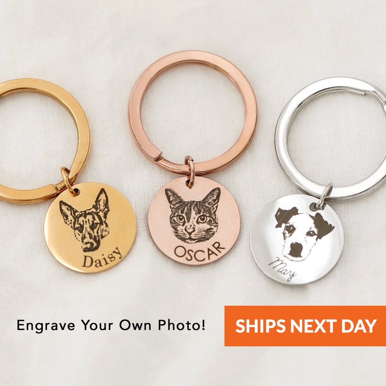 May include: Three personalised keychains with engraved images of pets. The keychains are gold, rose gold, and silver. The engraved images are of a dog, a cat, and a dog. The keychains are labelled "Daisy", "Oscar", and "Max".