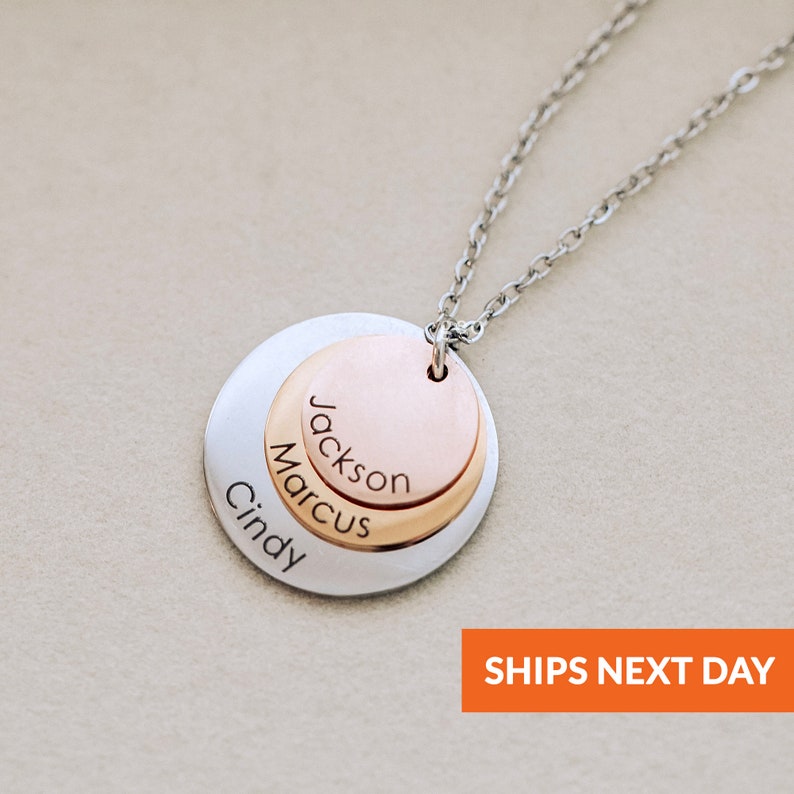May include: A silver chain necklace with a layered pendant featuring three engraved names: Cindy, Marcus, and Jackson. The top layer is rose gold.