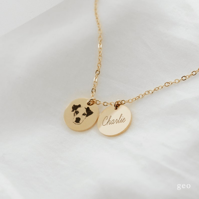 Op de afbeelding: Gouden ketting met twee ronde hangers. Een hanger heeft een zwart-wit foto van een hond, de andere hanger heeft de naam "Charlie" gegraveerd.