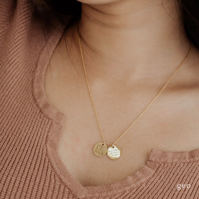 May include: A gold chain necklace with two round pendants. One pendant features a state outline and the other pendant has the text "You are my sunshine, my only sunshine, you make me happy when skies are gray".