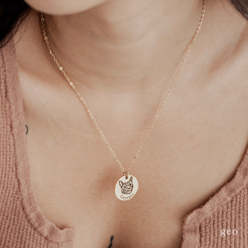 May include: A gold chain necklace with a round pendant featuring a pet's engraved portrait and the name "Georgie".