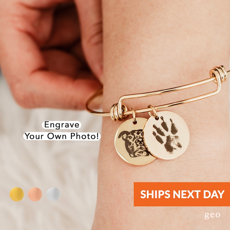 May include: Gold expandable bracelet with two charms. One charm features a paw print and the other charm features a dog's face.  Engrave Your Own Photo!  SHIPS NEXT DAY