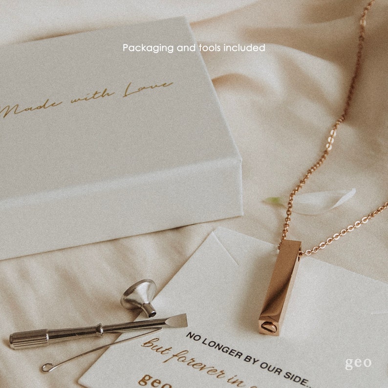 May include: A gold necklace with a rectangular pendant that has a small opening on the side. The necklace is packaged in a white box with the words "Made with Love" on the top. The package also includes a small funnel, a screwdriver, and a small tool for opening the pendant. The card says "No longer by our side, but forever in our hearts."