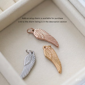 May include: Three angel wing charms in different metal finishes: silver, gold, and rose gold. The charms are displayed in a white box.