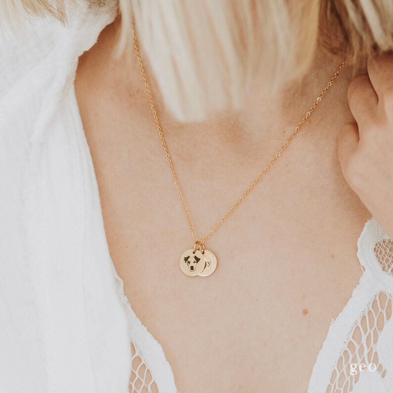 Op de afbeelding: Een gouden ketting met twee bedels. De eerste bedel is een ronde schijf met een uitgesneden wereldkaart. De tweede bedel is een ronde schijf met de letter "Y" erop gegraveerd.