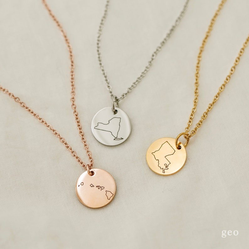 May include: Three necklaces with different state outlines on circular pendants. The necklaces are silver, gold, and rose gold. The states are New York, Maine, and Hawaii.