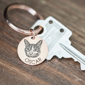 May include: A rose gold key ring with a round copper tag featuring a black and white photo of a cat with the name "OSCAR" engraved below.