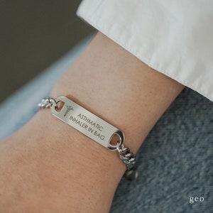 May include: Silver medical alert bracelet with a chain link band and a rectangular tag that reads "ASTHMATIC INHALER IN BAG". The tag also features a small medical symbol.