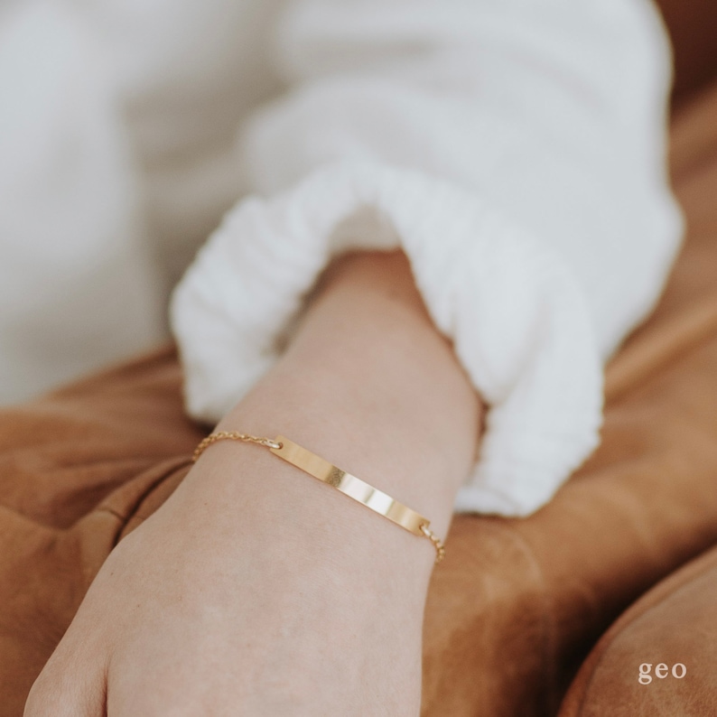 May include: A gold chain bracelet with a thin, flat, rectangular bar charm.