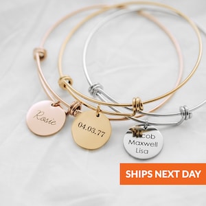 May include: Three gold bangle bracelets with engraved charms. The charms are round and feature the names "Rosie", "04.03.77", and "Jacob Maxwell Lisa".