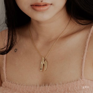 May include: Gold necklace with a small wing charm and a bar pendant engraved with the text "3.11.10 - 6.18.20" and a paw print.