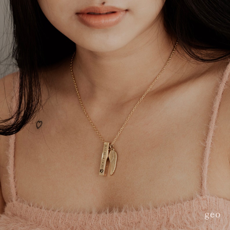 May include: Gold necklace with a small wing charm and a bar pendant engraved with the text "3.11.10 - 6.18.20" and a paw print.