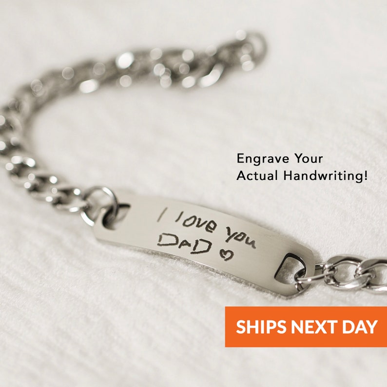 Puede incluir: Un brazalete de cadena de plata con una etiqueta rectangular grabada con el mensaje escrito a mano "Te quiero pap&aacute;" y un s&iacute;mbolo de coraz&oacute;n.