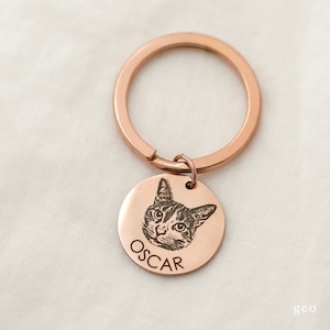 May include: Rose gold keyring with a round engraved tag featuring a cat's face and the name "OSCAR".