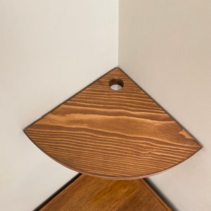 May include: A wooden corner shelf with a rounded edge and a hole in the center. The shelf is stained a dark brown color.