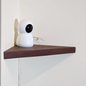 Op de afbeelding: Een witte beveiligingscamera met een zwarte lens staat op een donkerbruin hoekplank.