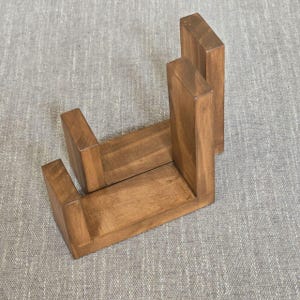 May include: A wooden, U-shaped shelf with a warm brown finish. The shelf is constructed from rectangular pieces of wood, creating a sturdy and minimalist design. The shelf is designed to stand upright.