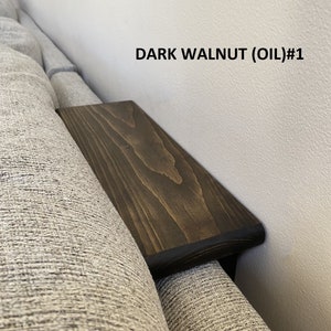 May include: A dark walnut stained wooden sofa arm tray with a black edge. The tray is attached to the arm of a gray sofa. The text "DARK WALNUT (OIL)#1" is visible in the image.