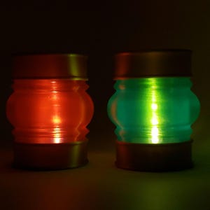 May include: Two decorative glass candle holders with a gold rim. The candle holder on the left is filled with a red candle and the candle holder on the right is filled with a green candle.