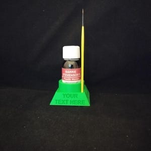 Può includere: Supporto in plastica verde con una piccola bottiglia di colla a solvente liquido Plastik Welder di Barrie Stevenson e un pennello giallo. Il supporto ha il testo "YOUR TEXT HERE" stampato.