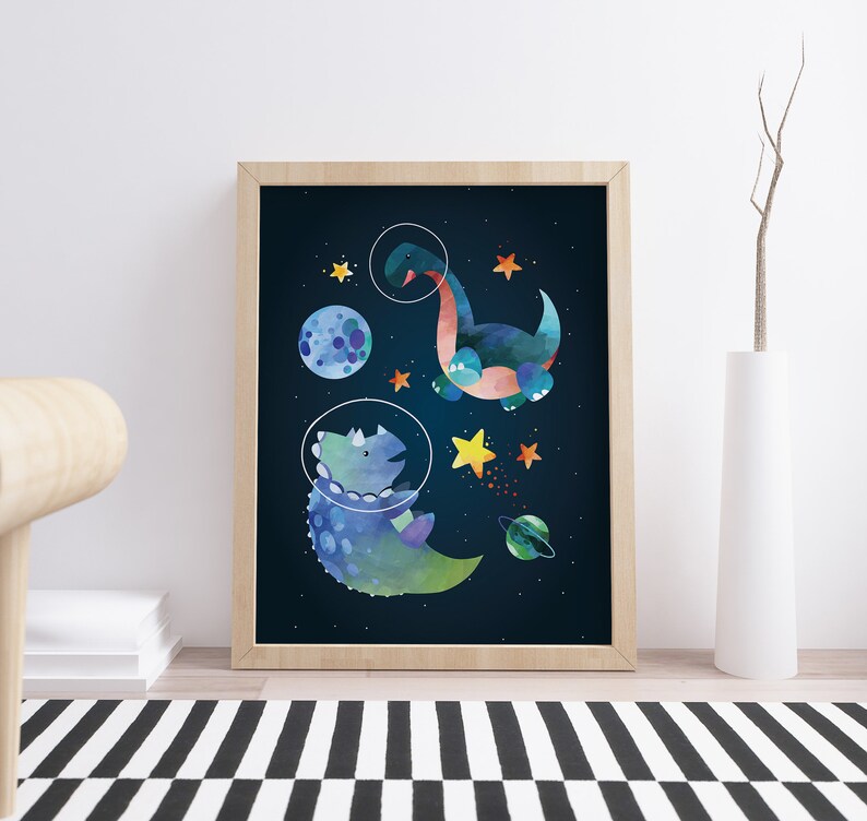 May include: A framed print of two dinosaurs in space. One dinosaur is blue and green and is wearing a space helmet. The other dinosaur is blue and orange and is floating in space. The background is a dark blue with stars and planets.