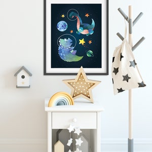 May include: A framed print of two dinosaurs in space suits floating in space with stars and planets. The print is hanging on a white wall above a white bedside table with a rainbow stacking toy, a star-shaped nightlight, and a string of white stars hanging from the bottom shelf.
